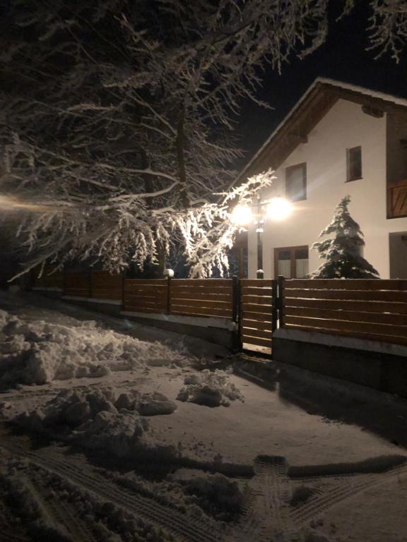 uma casa com uma cerca na neve à noite em Casa de vacanta Mogosa em Baia-Sprie