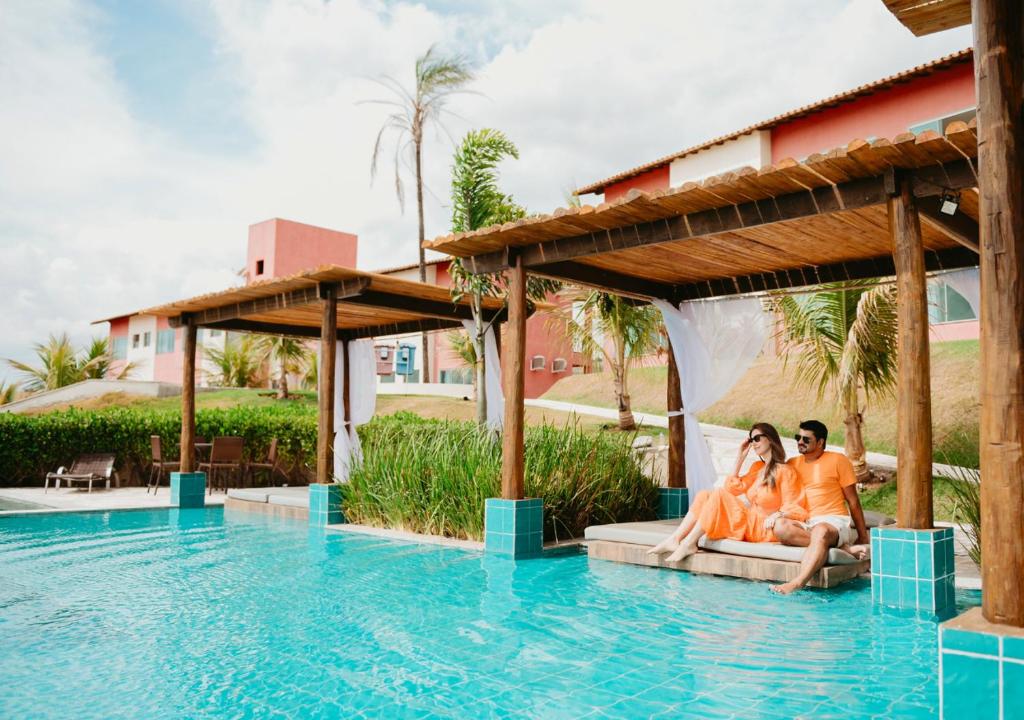 una pareja sentada en el borde de una piscina en un complejo en Hotel Chalé Capitólio en Capitólio