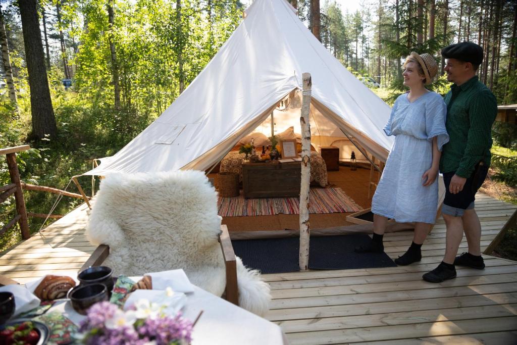 Un uomo e una donna in piedi davanti a una tenda di Karkausmäki Glamping a Kinnula