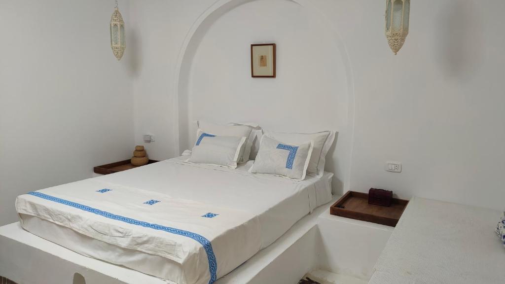 Dormitorio blanco con cama con sábanas y almohadas blancas en Maison d’hôte, Djerba 