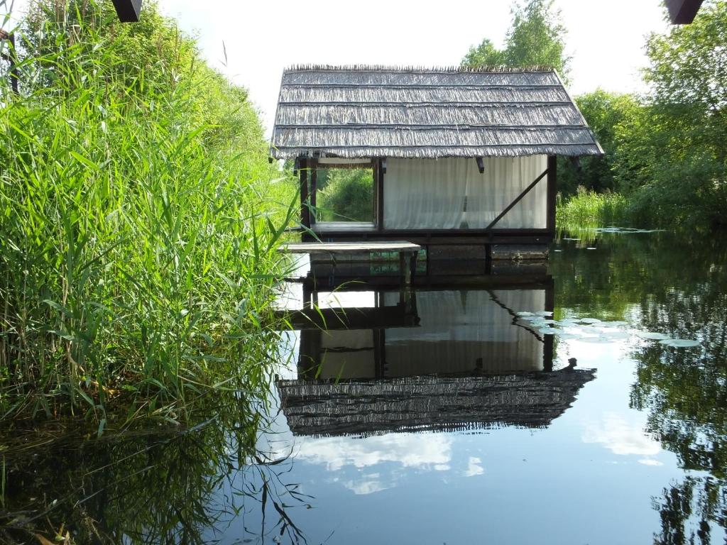 een klein gebouw op het water naast wat gras bij Camping Zanzibāra in Ķekava