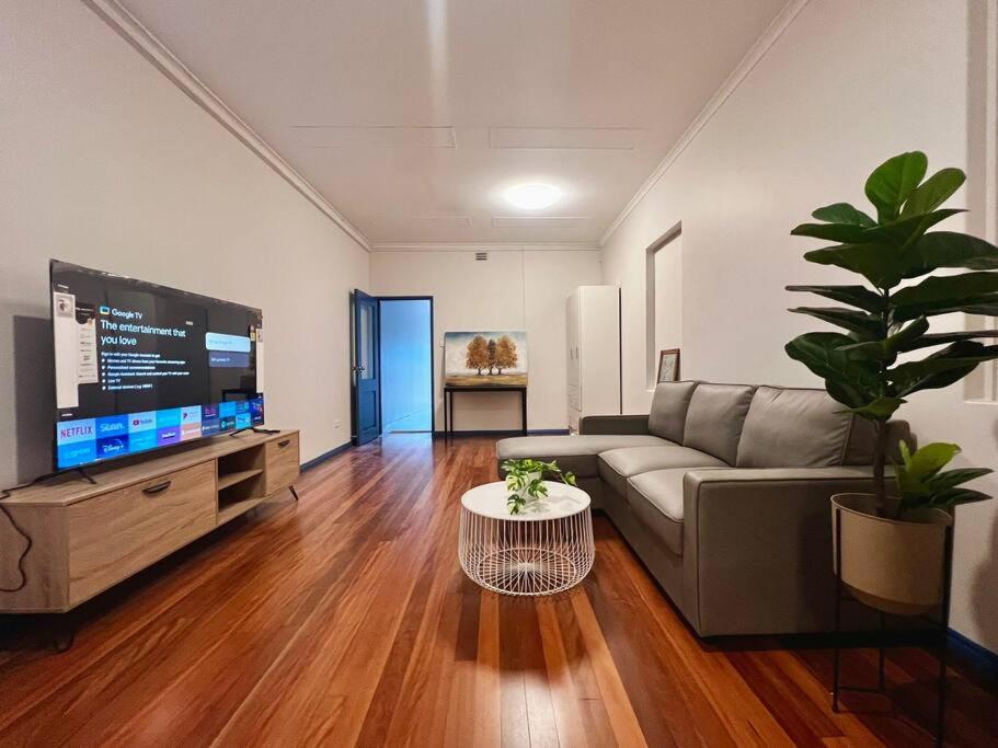 Il comprend un salon doté d'un canapé et d'une télévision à écran plat. dans l'établissement 3 Bedroom Cozy Stay 5km CBD, à Sydney