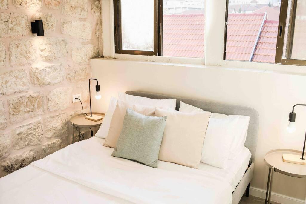 1 cama blanca con almohadas en una habitación con ventanas en Gabriel Apartments - Stone Suits JEM City Center, en Jerusalén