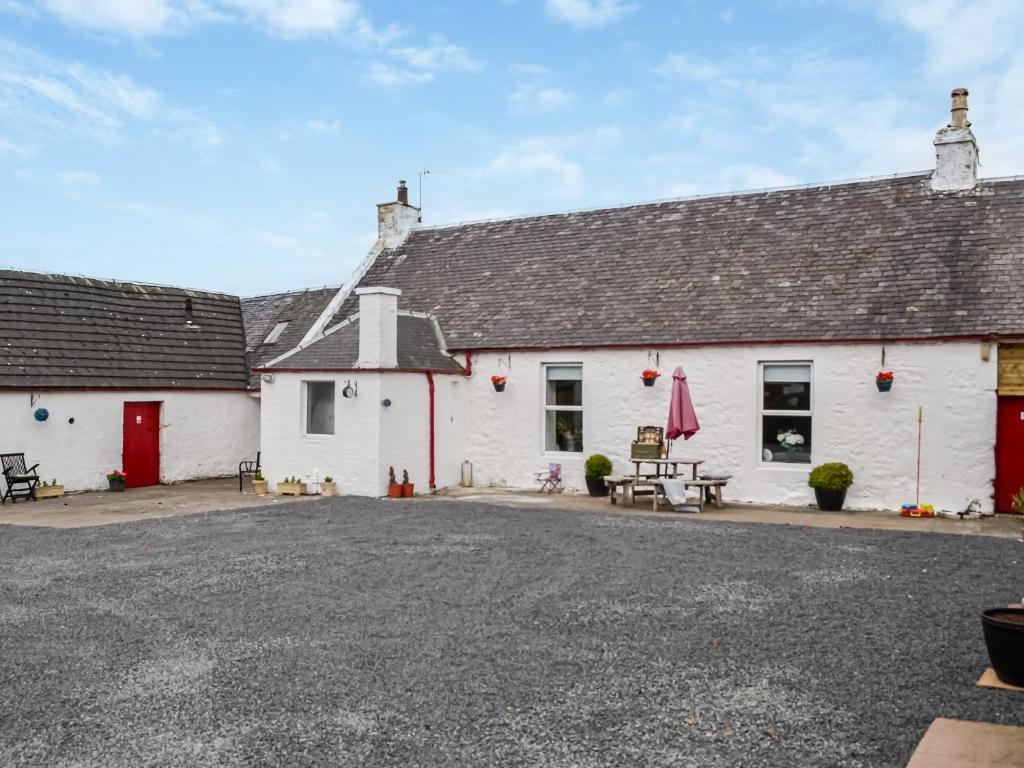 a white building with red doors and a parking lot at Muirston Farmhouse in Ochiltree