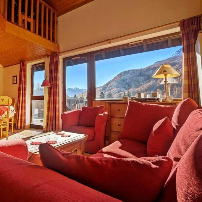 Elle comprend un salon doté d'un mobilier rouge et d'une grande fenêtre. dans l'établissement L'Hermine - Duplex à 5mn des pistes avec garage, à Saint-Chaffrey