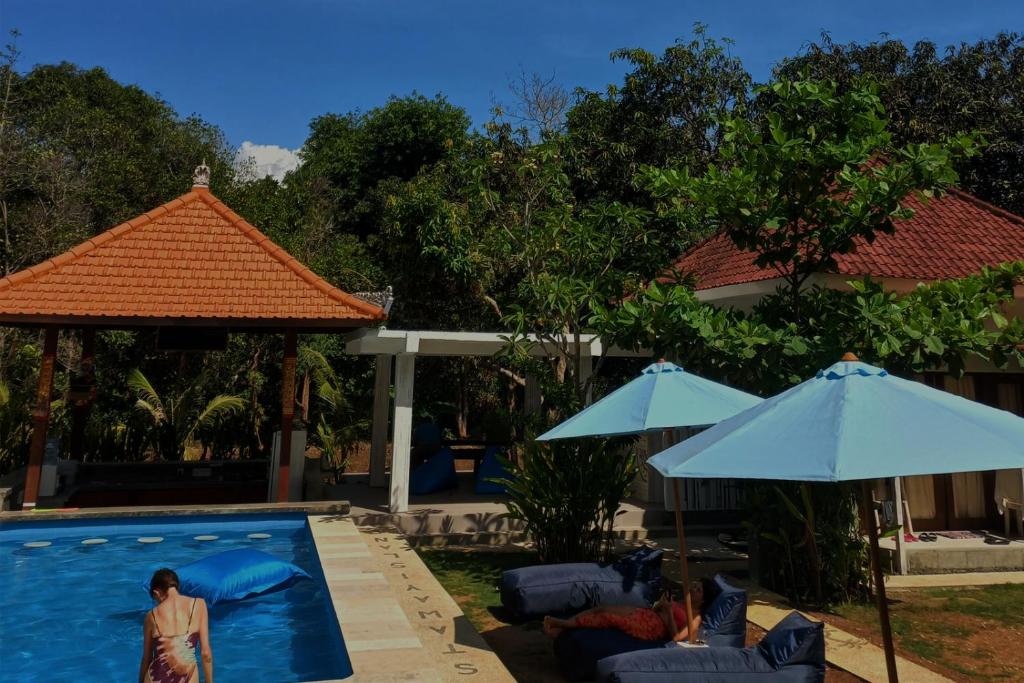 a woman standing next to a swimming pool with two umbrellas at Castaway Island Hostel in Nusa Lembongan