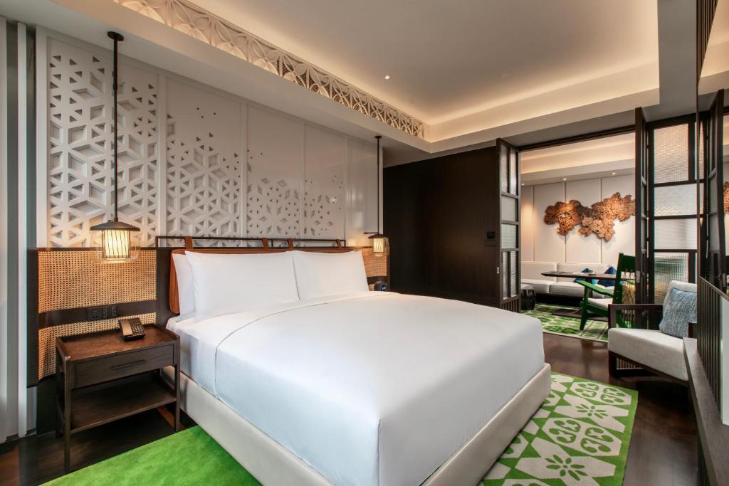 A king bedroom opening toward a separate sitting area with a green rug and city-facing window.