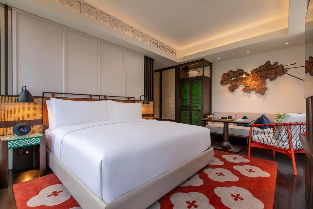 A king bed anchors a warmly styled bedroom with a compact table and two red chairs.