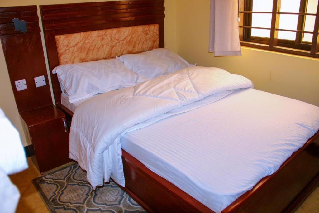 - un lit avec des draps blancs et une tête de lit en bois dans l'établissement Getaway bnb - Njombe, à Njombe