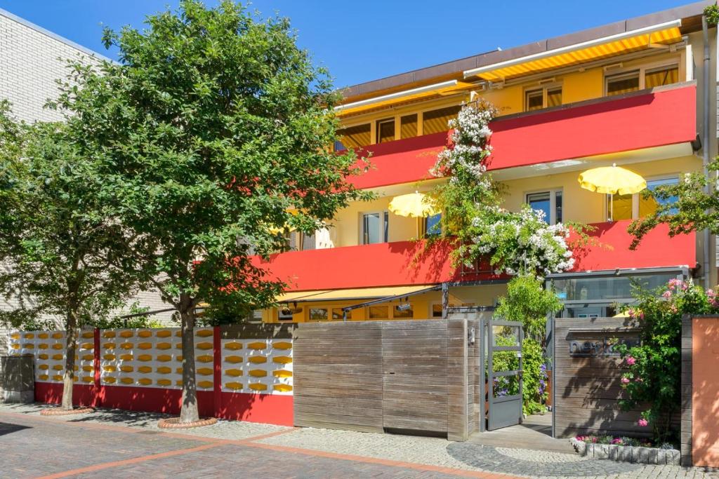 un edificio rosso e giallo con recinzione e alberi di neyland apartments Norderney a Norderney