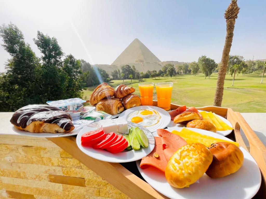 ein Tablett mit Frühstückslebensmitteln auf einem Tisch mit den Pyramiden in der Unterkunft Glamour Pyramids Hotel in Kairo