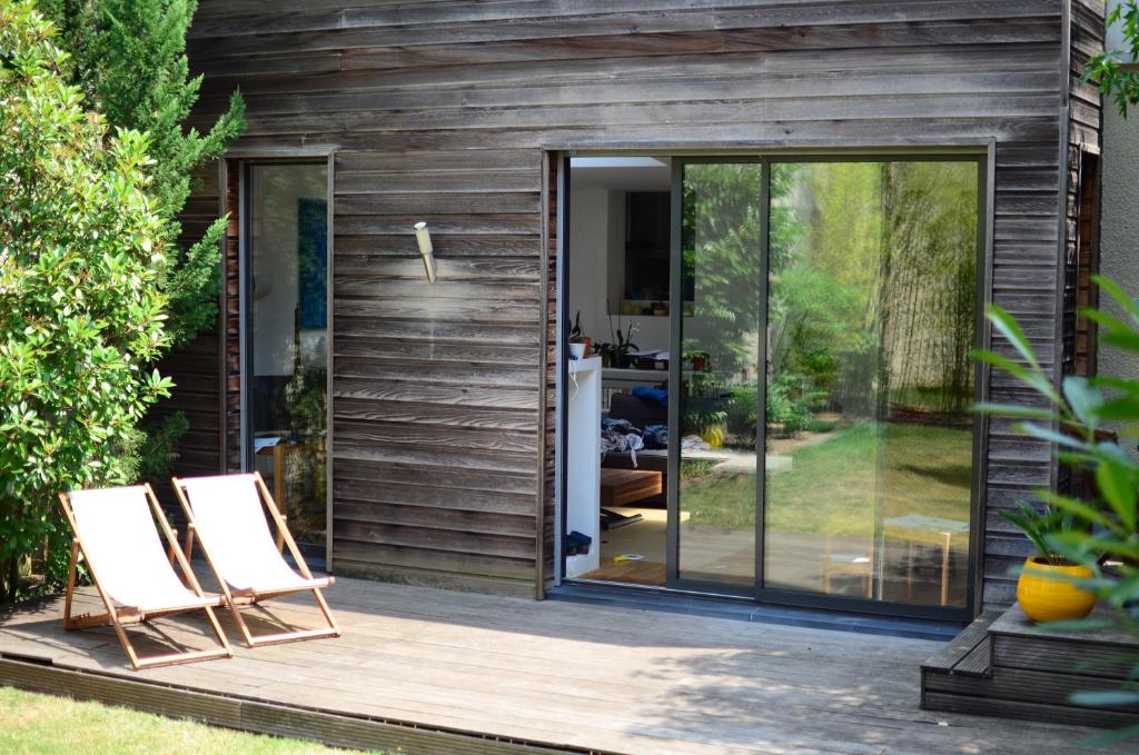 une maison avec des portes en verre et deux chaises sur une terrasse dans l'établissement Évasion Boisée à 2 pas des JO et de Paris, à Joinville-le-Pont