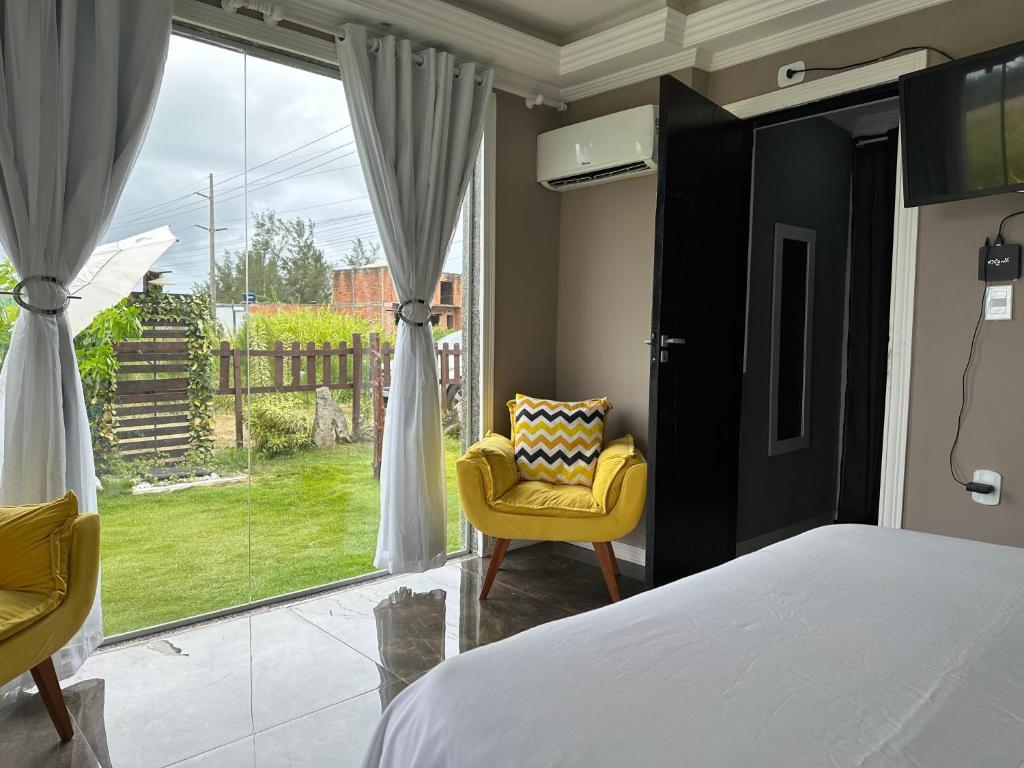 um quarto com uma cama e uma cadeira amarela e uma janela em Flat Restinga em Arraial do Cabo