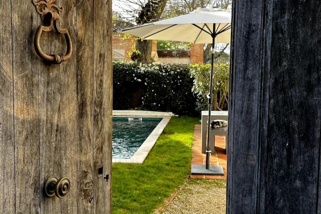 una puerta abierta con una sombrilla junto a una piscina en Maison de Charme Piscine & Piano, 30 min Toulouse, en Loubens-Lauragais