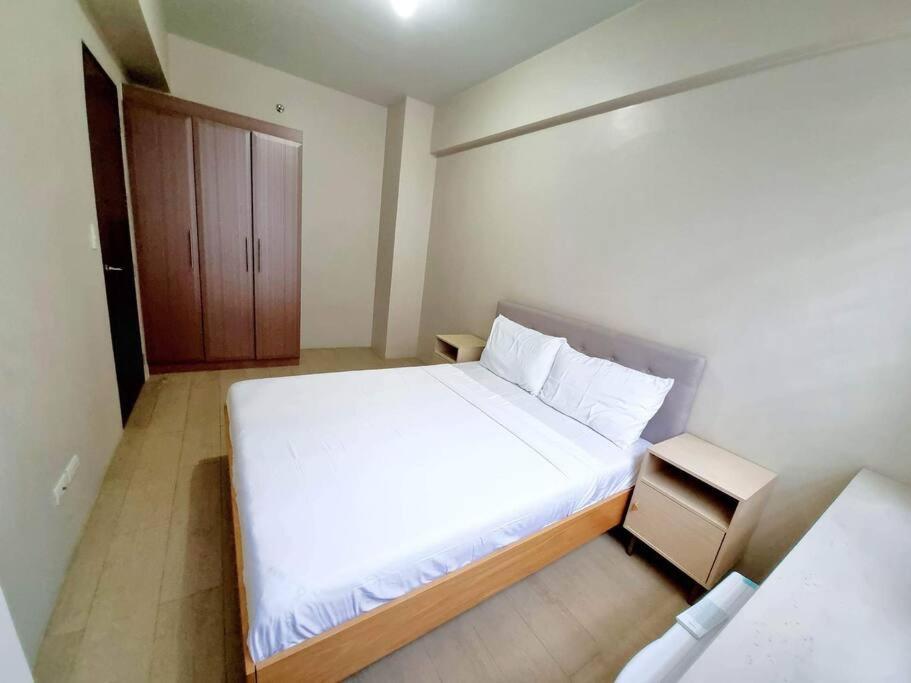 ein kleines Schlafzimmer mit einem weißen Bett und einem Holzschrank in der Unterkunft Condo in Pasay in Manila