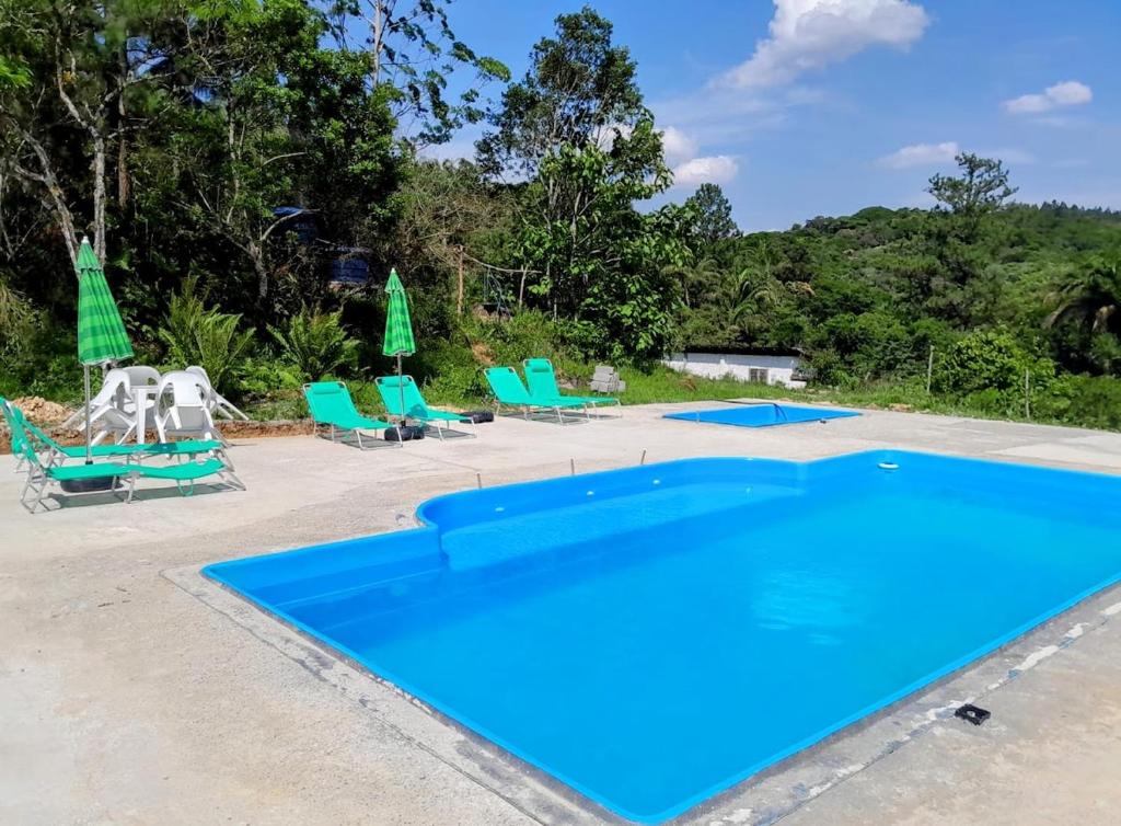 a blue swimming pool with chairs and umbrellas at Casas de Campo Beija-Flor & Bem-Te-Vi, Mata Atlântica, Juquitiba, SP in Juquitiba