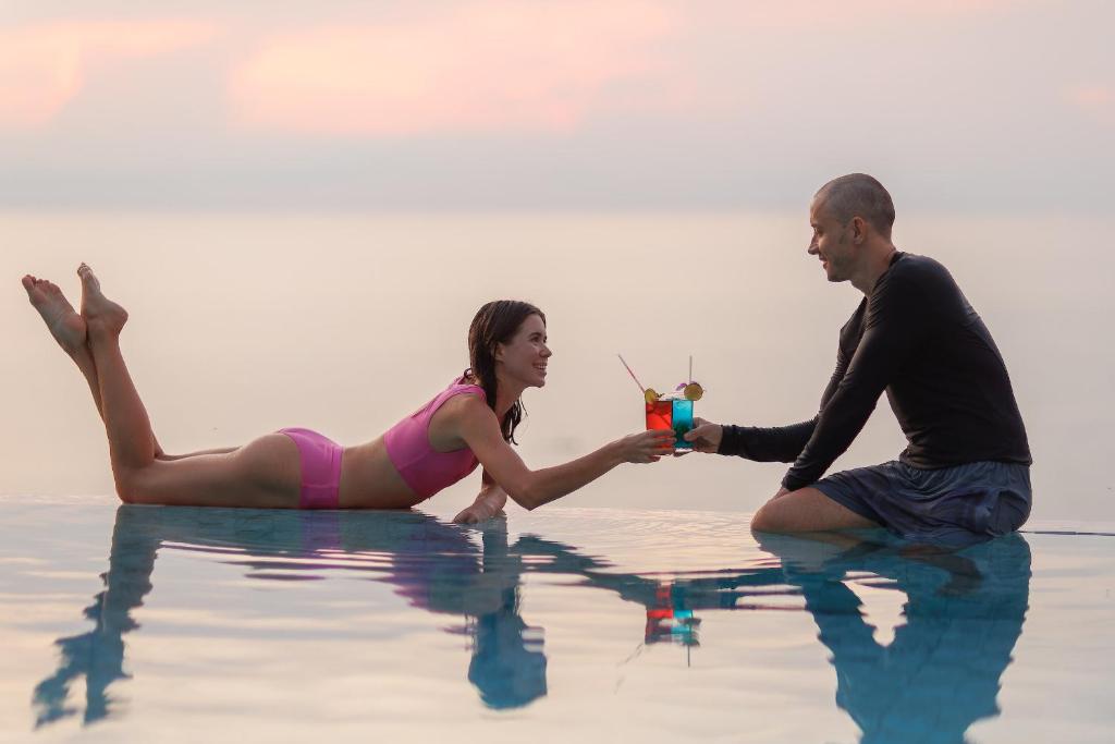 Ein Mann und eine Frau, die auf dem Wasser sitzen und Getränke halten. in der Unterkunft The Dreaming View Villa in Haad Yao