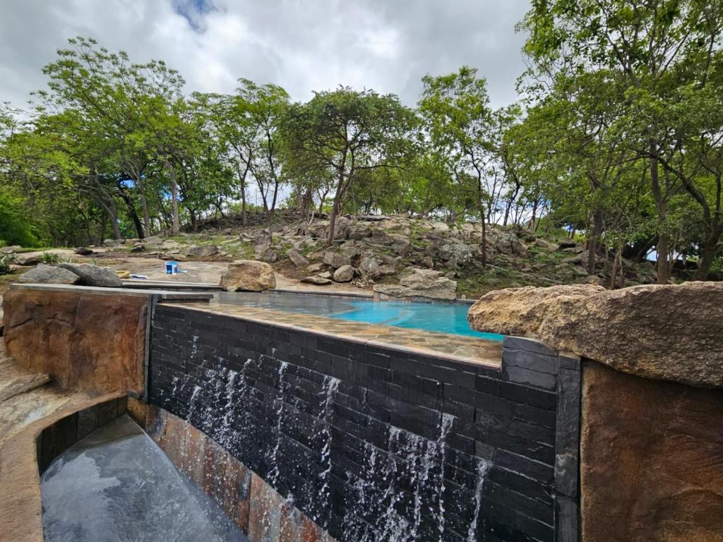a swimming pool with a waterfall in front of a mountain at GEORGE B BOUTIQUE LODGE in Tzaneen