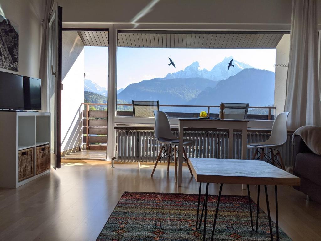 a living room with a table and a balcony with mountains at Haus Mitterbach Ferienwohnung Berglaune in Berchtesgaden