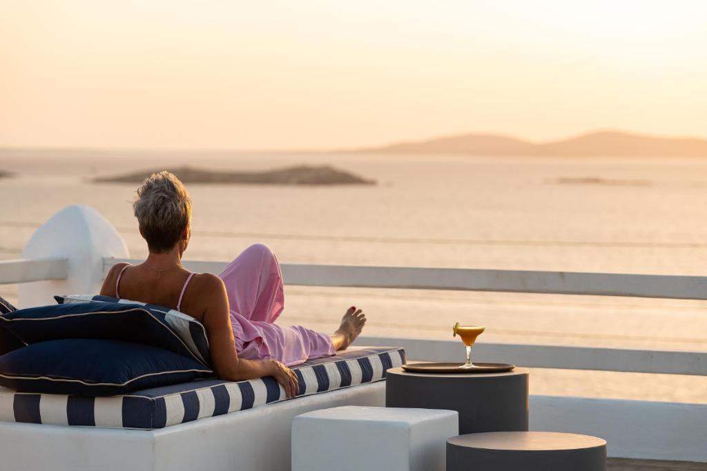 Un uomo seduto su una chaise longue che guarda l'oceano di Hotel Tagoo a Mykonos Città