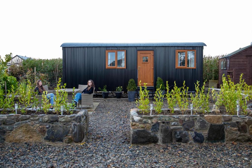 a black tiny house with people sitting in the yard at Carlingford Glamping Hut 