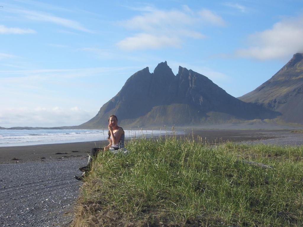 a person sitting on a beach with a mountain in the background at Lón Guesthouse in Thorgeirsstadir