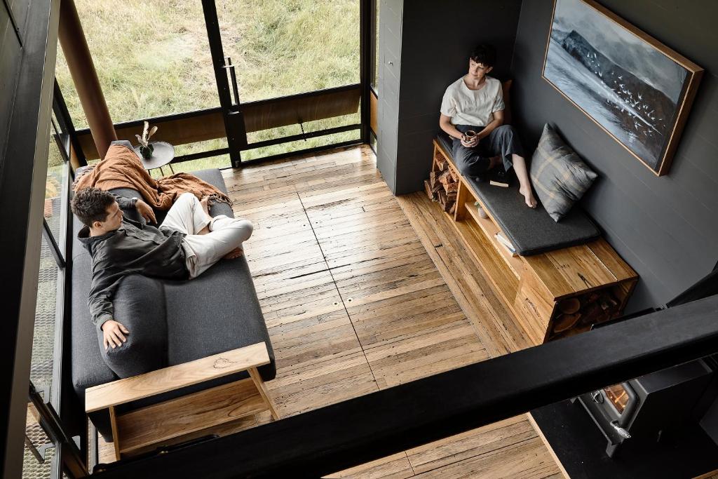 two men sitting on a couch in a room at A Small, Off-Grid farm house with ocean views. in Illowa