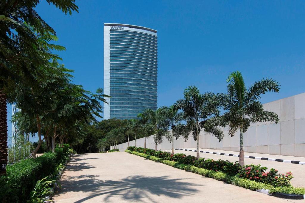 a tall building with palm trees and a sidewalk at The Westin Mumbai Garden City in Mumbai