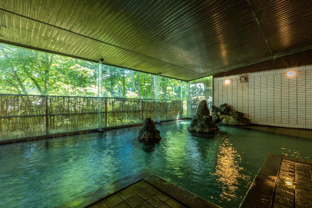 a pool of water in a room with rocks in it at KAMENOI HOTEL Tazawako in Senboku