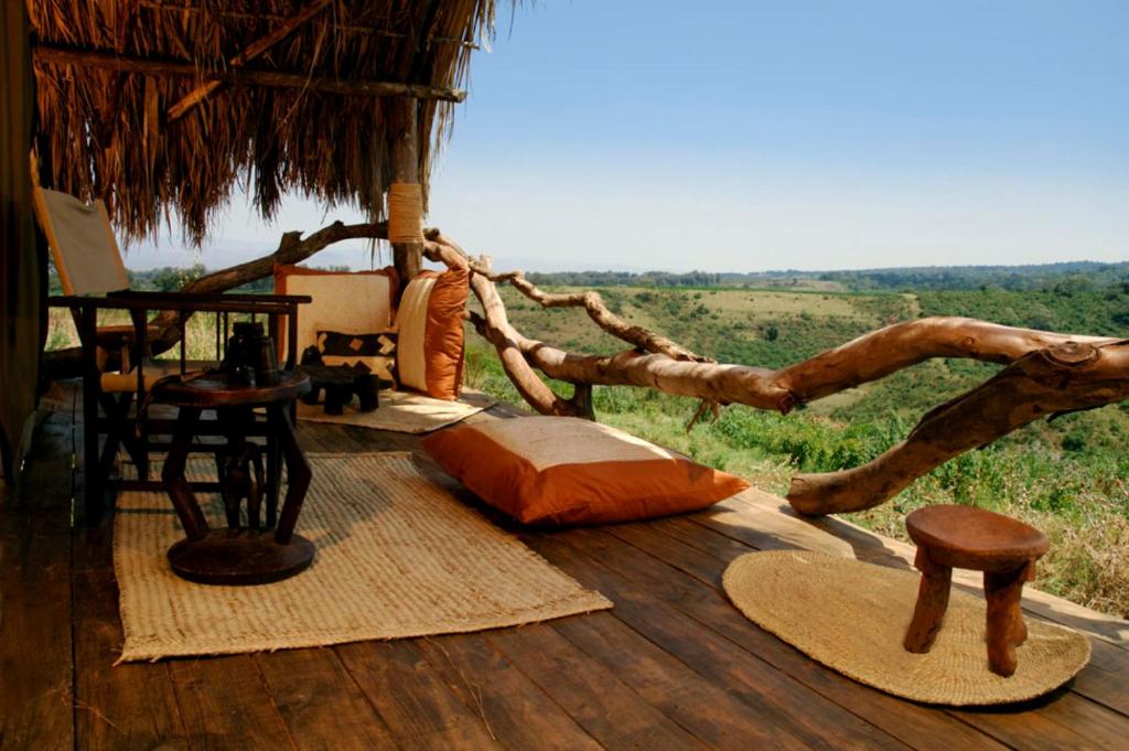 una terraza de madera con cama, mesa y sillas en Crater Forest Tented Lodge, en Karatu