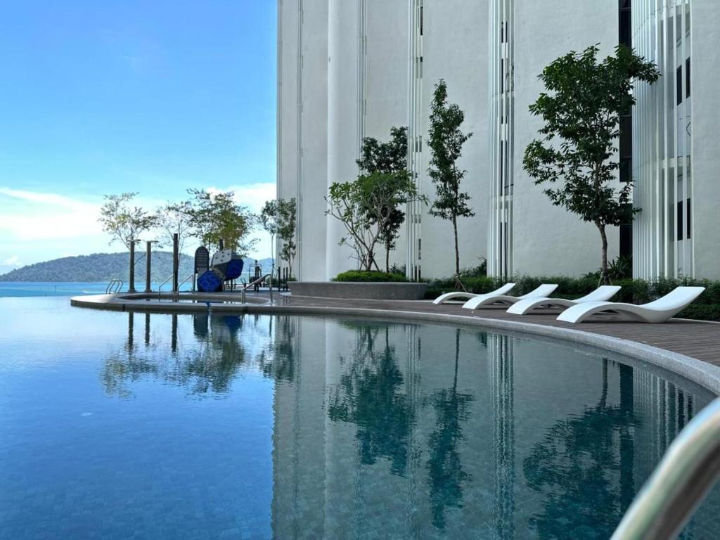 a swimming pool with white chairs next to a building at The Shore Kota Kinabalu by Ariana in Kota Kinabalu