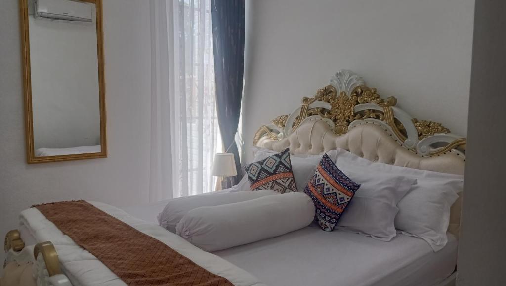 Cama blanca con cabecero y almohadas de oro y blanco en Arsya Bagas Villa, en Bogor