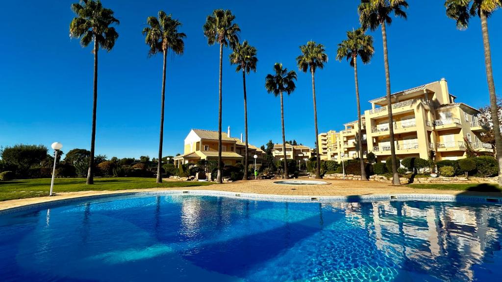 a swimming pool in front of a building with palm trees at Ellegance by Check-in Portugal in Vilamoura