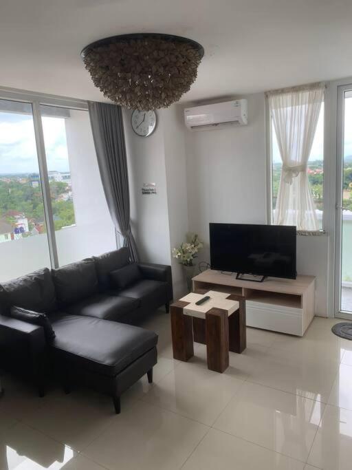 Una sala de estar con un sofá negro y un televisor. en 2BR VIVO Apartement by MJP, en Yogyakarta