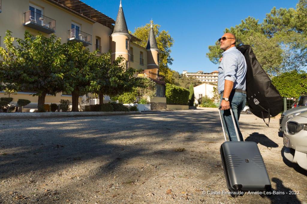a man with a suitcase standing next to a car at Appart'Hotel Castel Emeraude, Charme et Caractère in Amélie-les-Bains-Palalda