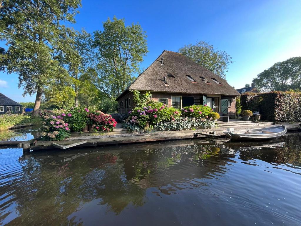 een huis met een rieten dak en bloemen op het water bij Plompeblad Suite Giethoorn in Giethoorn