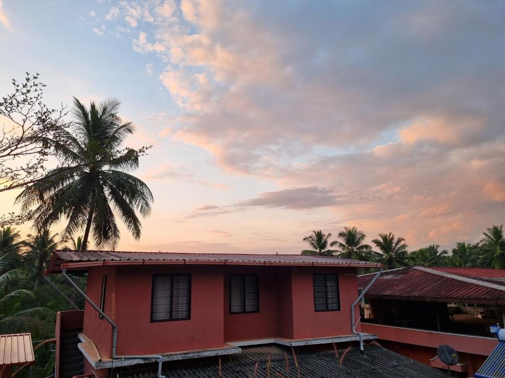 una casa con una palmera y un cielo nublado en Maison Parnakuti Adigas Homestay Dharmasthala Guest House Hotel Room, en Dharmastala