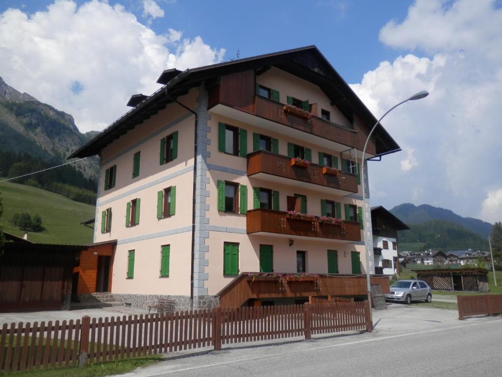 a building with green and white windows and a fence at Appartamenti Kratter Sara in Sappada