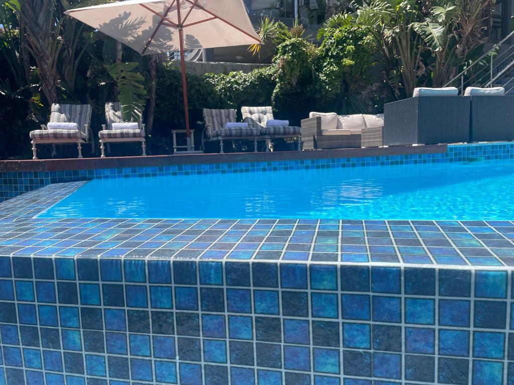 a swimming pool with a blue tile floor and an umbrella at Gull on the Bay Boutique Guest House in Bloubergstrand