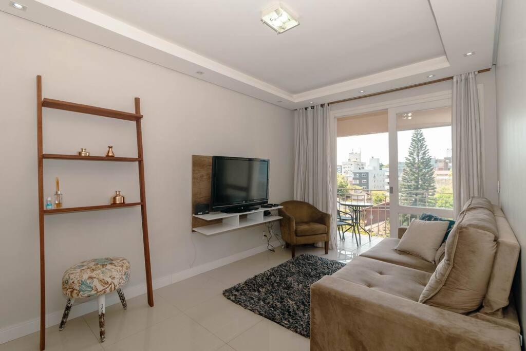 a living room with a couch and a television at Aps de frente com sacada ou terraço a 10 minutos do Aeroporto in Porto Alegre