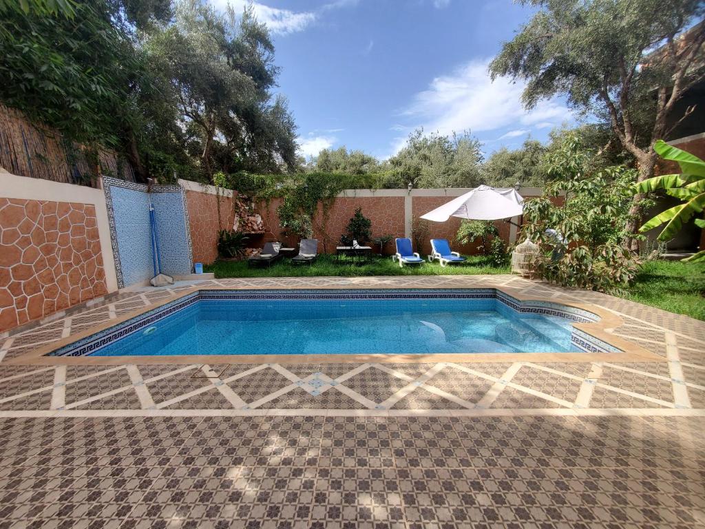 einen Pool in einem Garten mit Stühlen und einem Sonnenschirm in der Unterkunft Villas khadija in Marrakesch
