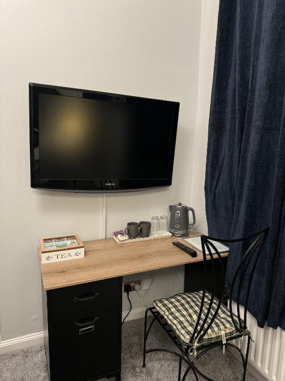 a desk with a television on a wall with a chair at Windsor Wine and Dine in Chertsey