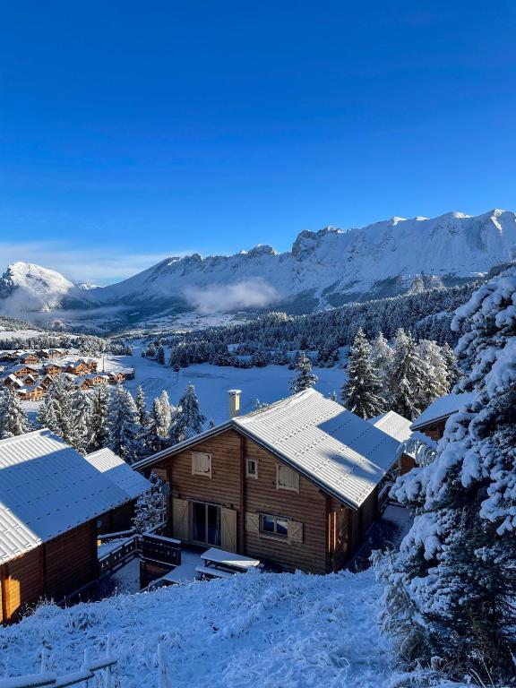 une cabane en rondins dans la neige avec des montagnes en arrière-plan dans l'établissement La joue du loup Bord des pistes - Chalet en bois de charme pour 10 personnes, à Saint-Étienne-en-Dévoluy