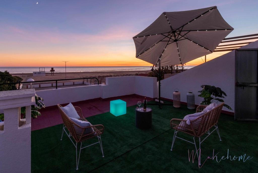 a patio with two chairs and an umbrella and the beach at Chalet en la misma playa in Punta Umbría