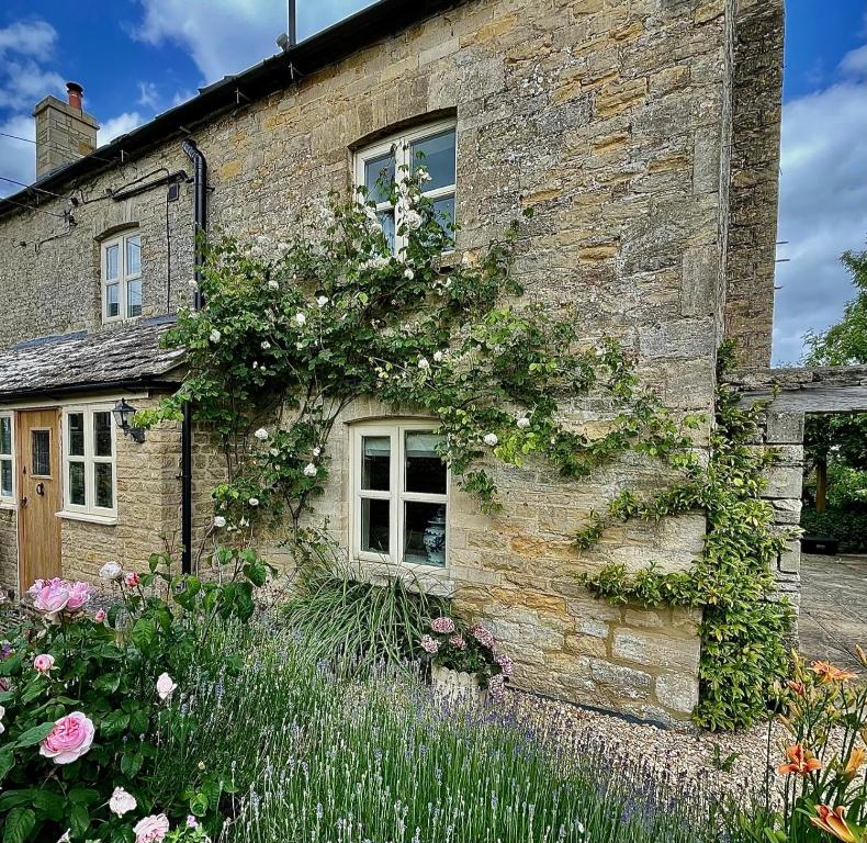 an old stone house with flowers on the side of it at Cosy Cotswold Cottage with garden Quenington near Bibury in Quenington