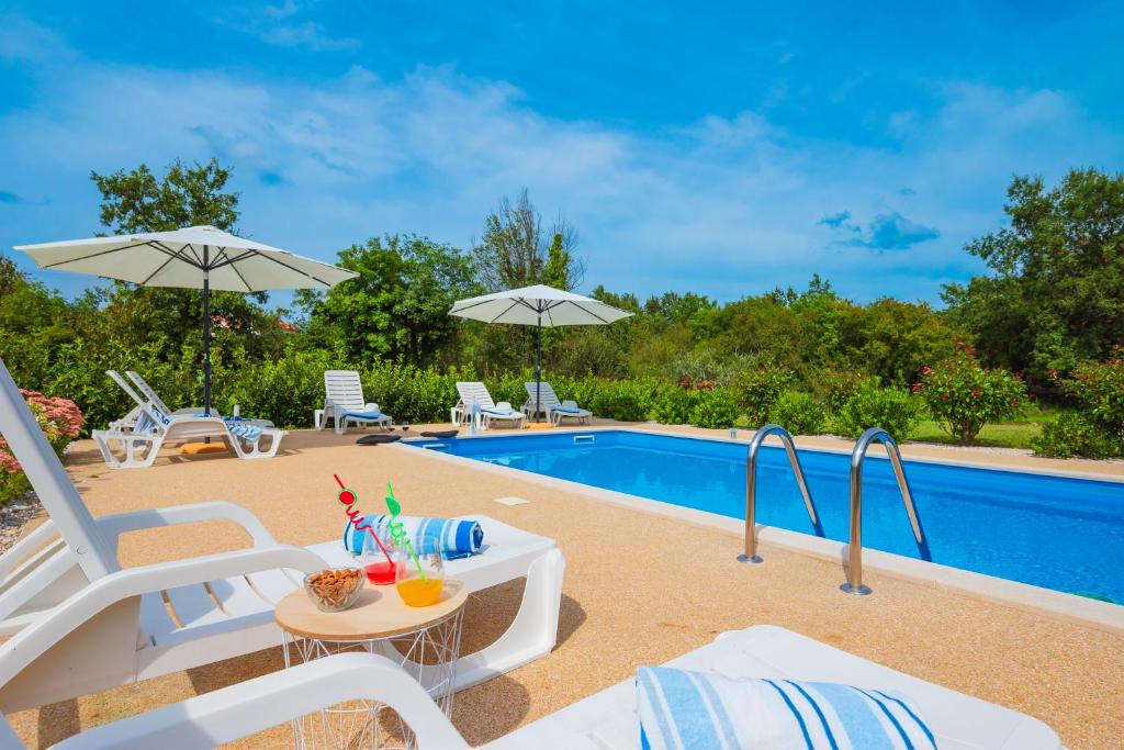 basen z białymi krzesłami i stołem z napojami w obiekcie Holiday Apartment Ariella w mieście Križanici