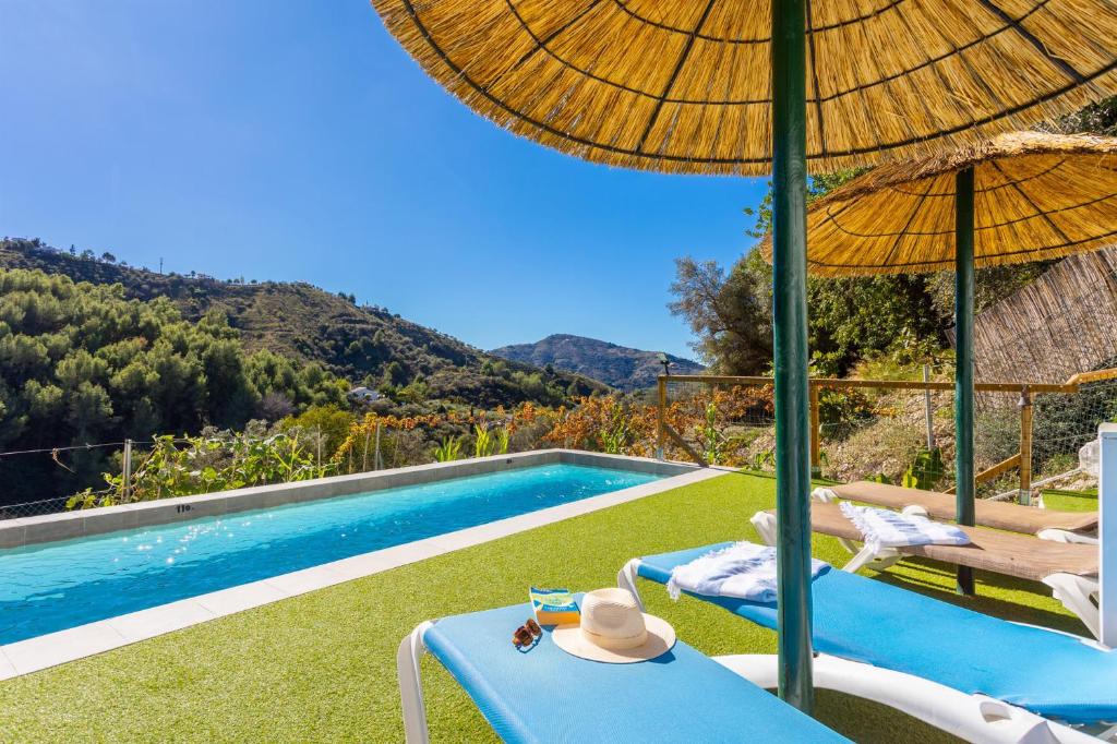 een villa met een zwembad met stoelen en een parasol bij Villa Flower in Cómpeta