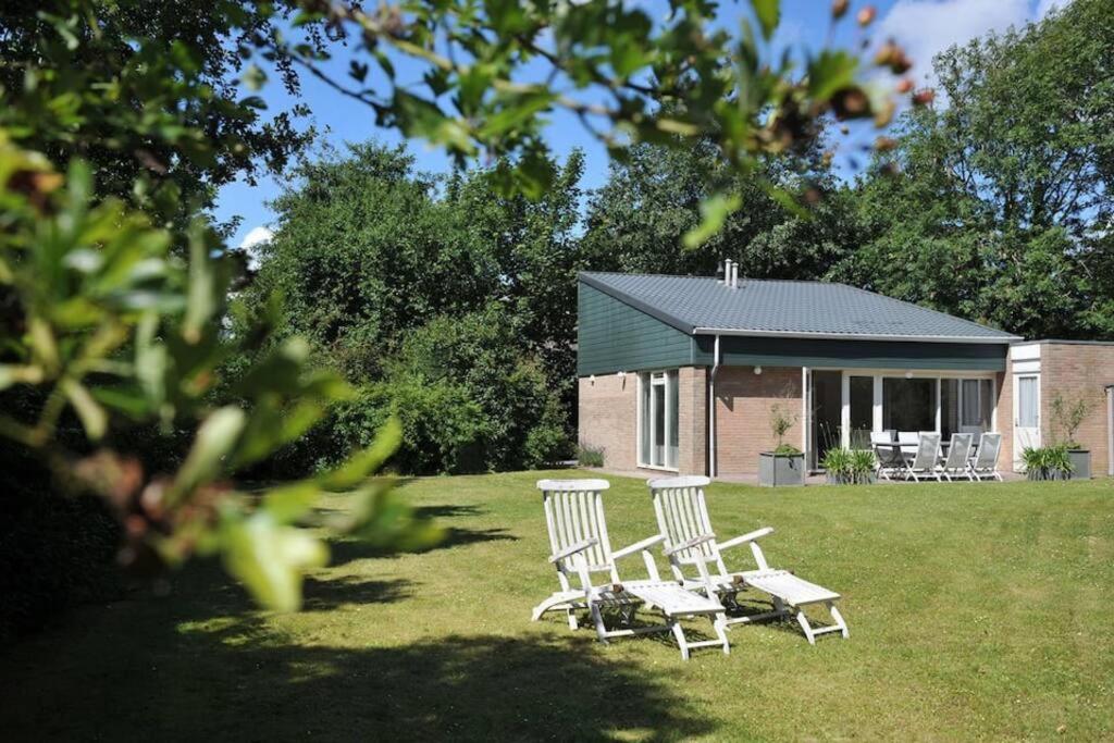 two chairs and a table in a yard with a house at Vrijstaand vakantiehuis, 5 minuten lopen van het strand in Zoutelande