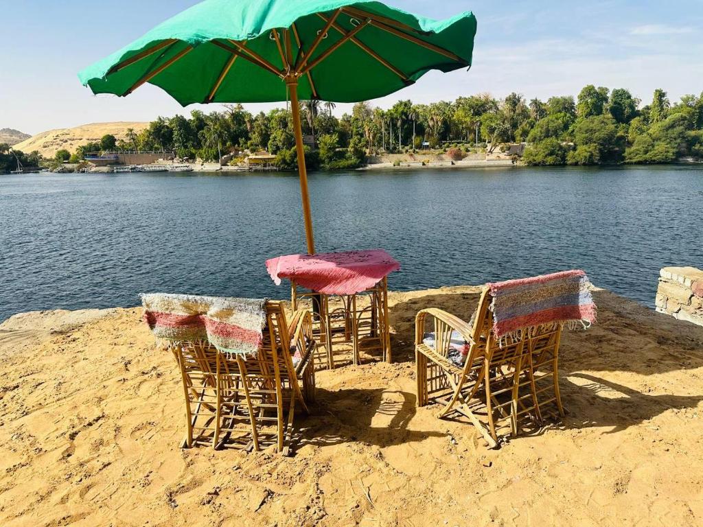 Nubian Bride guest house في أسوان: مجموعة من الكراسي ومظلة على الشاطئ