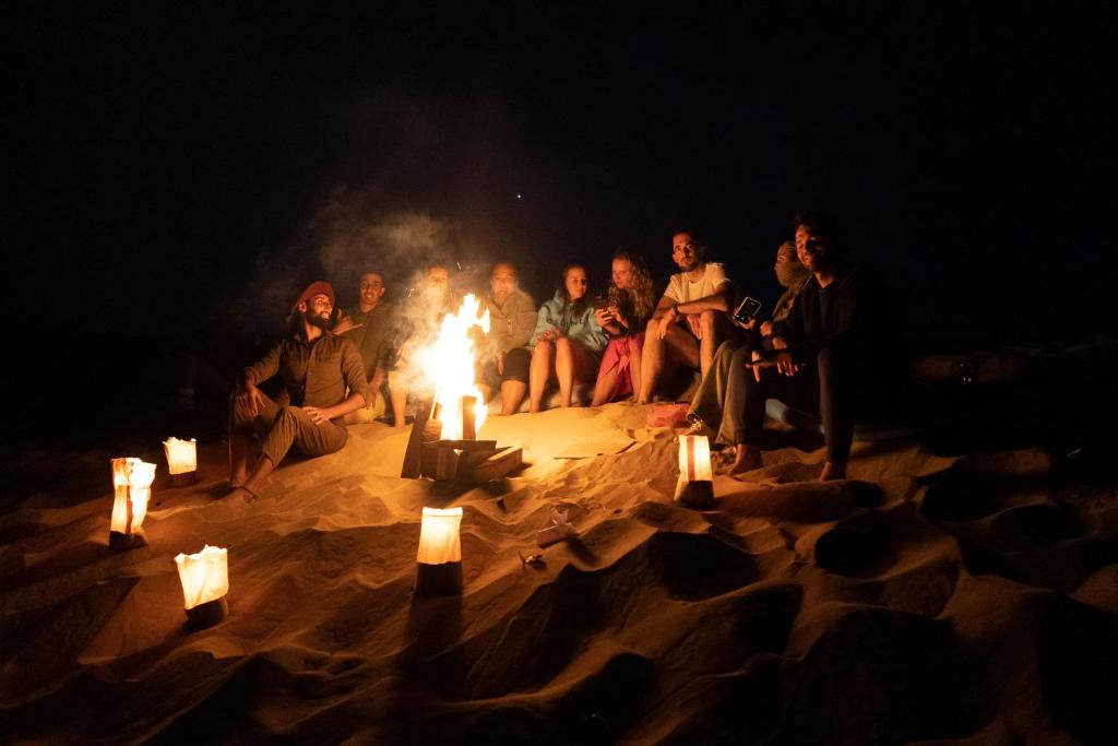 een groep mensen die rond een vuur in het zand zitten bij darna surf house anza in Agadir